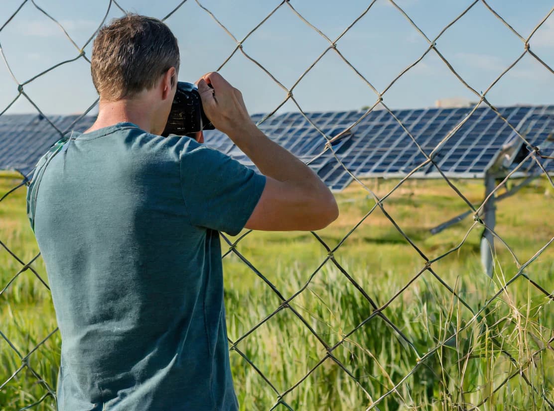 Unbefugter Mann fotografiert Solarpark hinter Zaun – Sicherheitsbedenken.