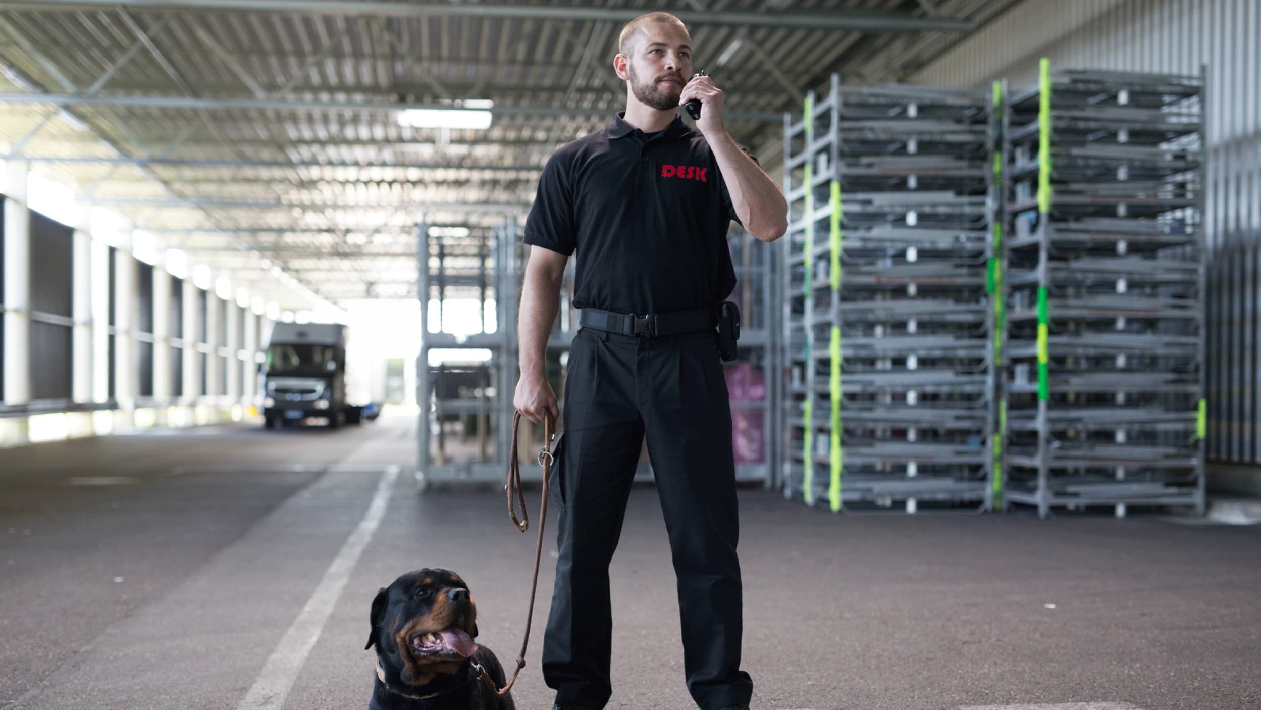 DESK-Sicherheitsmitarbeiter mit Schutzhund in Lagerhalle. Zuverlässige Sicherheit, Professionalität, Schutz.