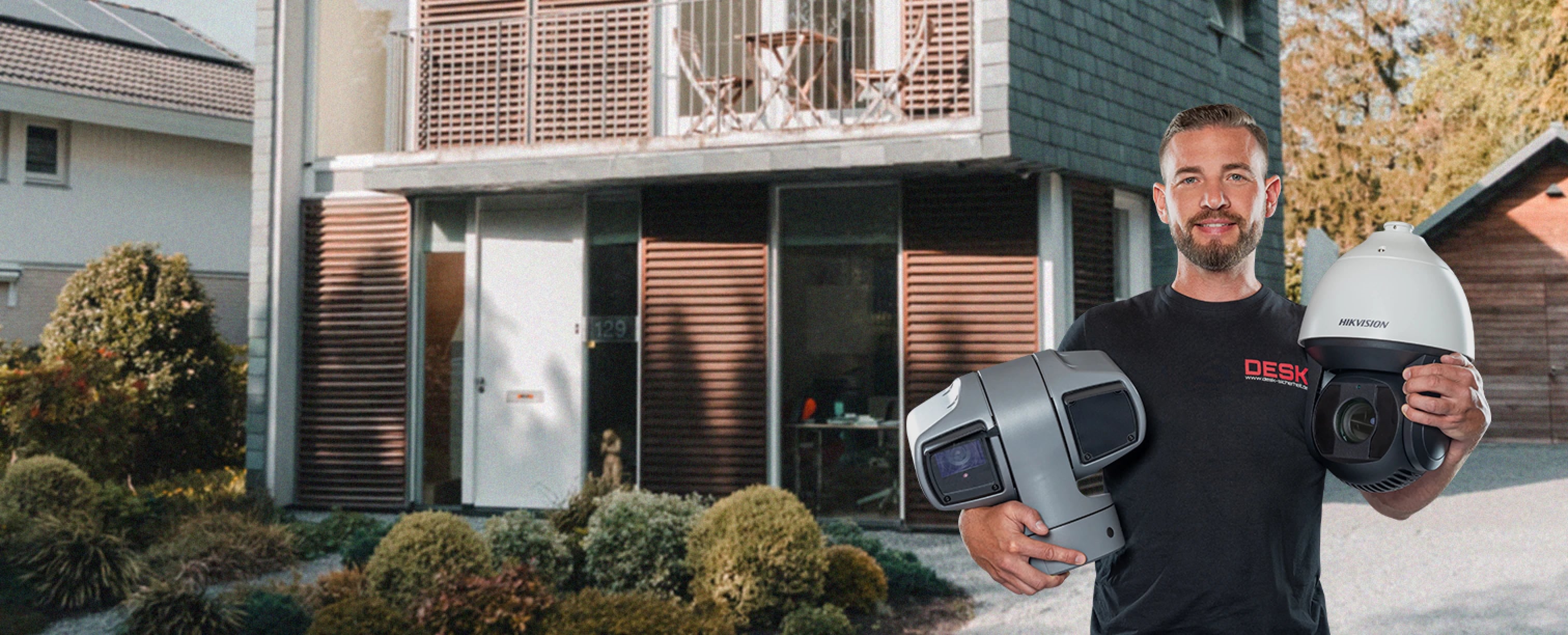 Sicherheitstechnik Videoüberwachung Zuhause: Techniker präsentiert Kameras vor einem Wohnhaus