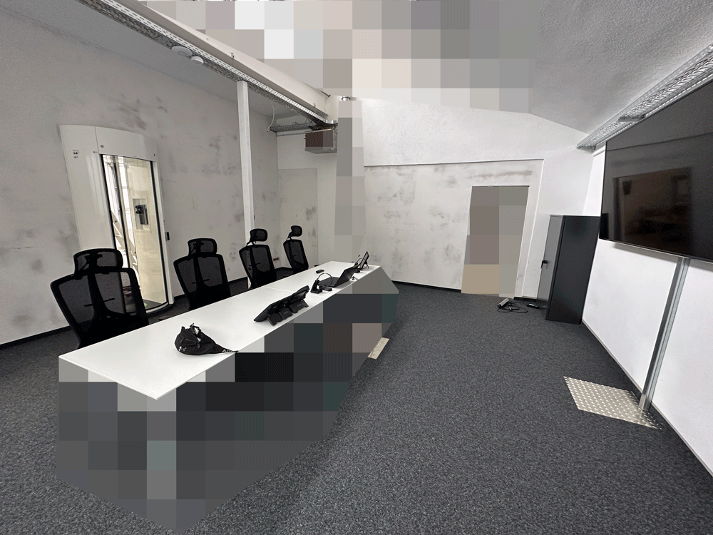 Innenansicht des Leitstellenraums der DESK Sicherheit in Karlsruhe mit Operator-Arbeitsplätzen, Bildschirmreihe und gesicherter Zugangsschleuse.